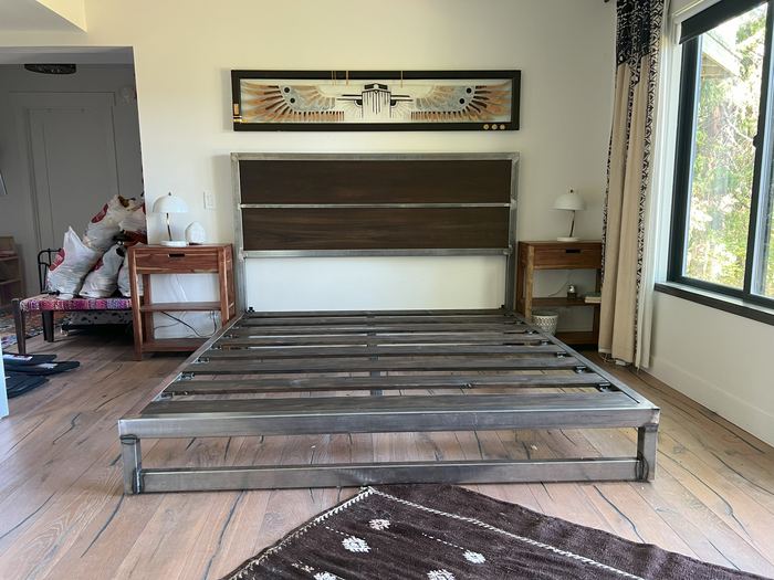 Welded steel bed frame with a wood-panel headboard in a bedroom