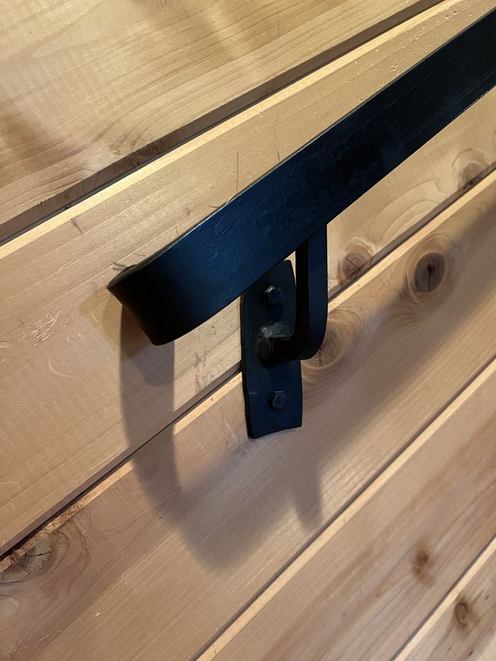 Black steel handrail on a cedar wall, held by a welded bracket