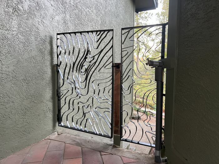 Pair of Topograin breezeway gates between stucco walls, with a wood-knot form in the pattern
