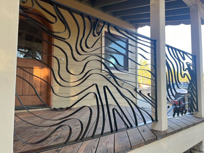 Black Topograin steel porch railing with flowing contour lines beside a wooden front door